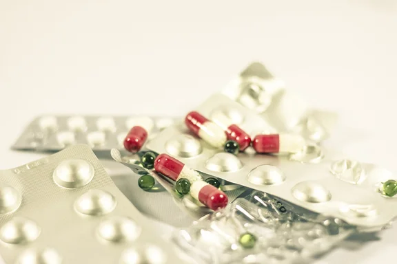 Verschiedene Medikamente – rote Kapseln, weiße Tabletten und geöffnete Blisterpackungen auf hellem Untergrund.
