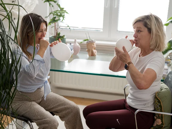 Atemübungen mit Luftballons Therapeutin und Patientin üben gemeinsam eine Atemübung mit weißen Luftballons in einem freundlichen Therapieraum.