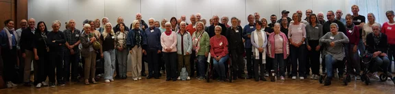 Gruppenfoto von mehr als 50 Teilnehmern des Patiententags 2024 des Lungenfibrose in Frankfurt am Main. Die Gruppe steht und sitzt in mehreren Reihen in einem hellen Veranstaltungssaal mit Parkettboden. Einige der Personen tragen Sauerstoffgeräte, zwei sitzen auf Rollatoren.
