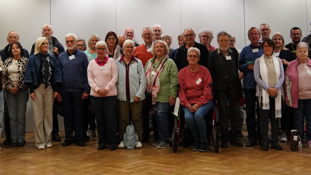 Gruppenfoto von mehr als 50 Teilnehmern des Patiententags 2024 des Lungenfibrose in Frankfurt am Main. Die Gruppe steht und sitzt in mehreren Reihen in einem hellen Veranstaltungssaal mit Parkettboden. Einige der Personen tragen Sauerstoffger&auml;te, zwei sitzen auf Rollatoren. 